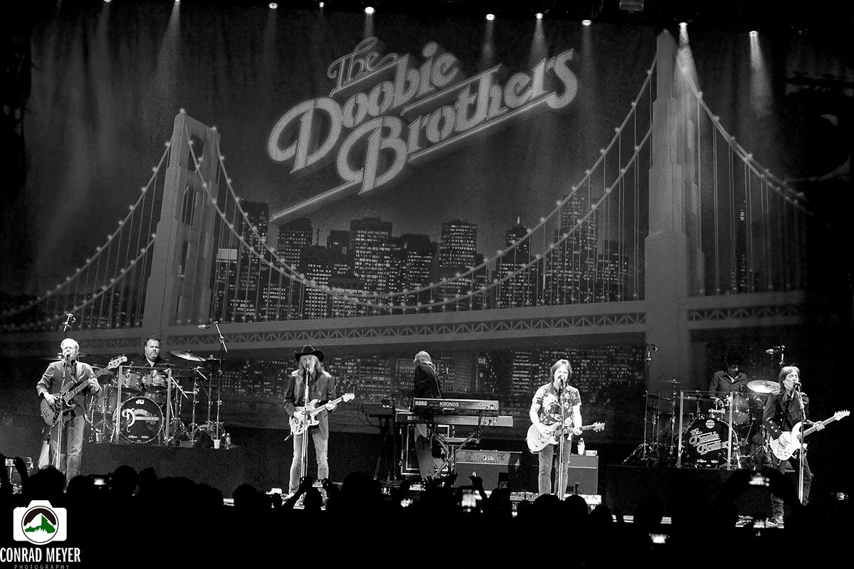 Band performing on stage with city backdrop.