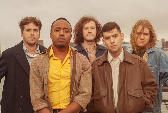 Five men standing outdoors, serious expressions.