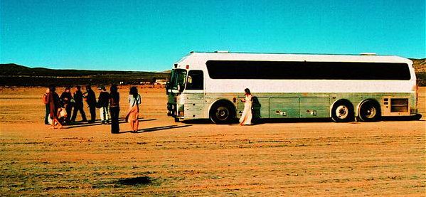 People near a bus in desert landscape.