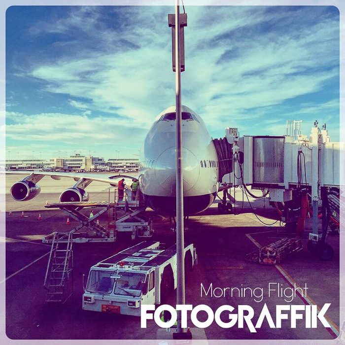 Airplane at airport gate under blue sky.