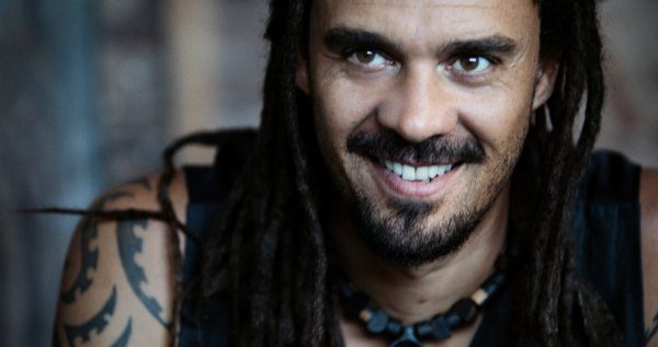Smiling person with dreadlocks and tattoos.