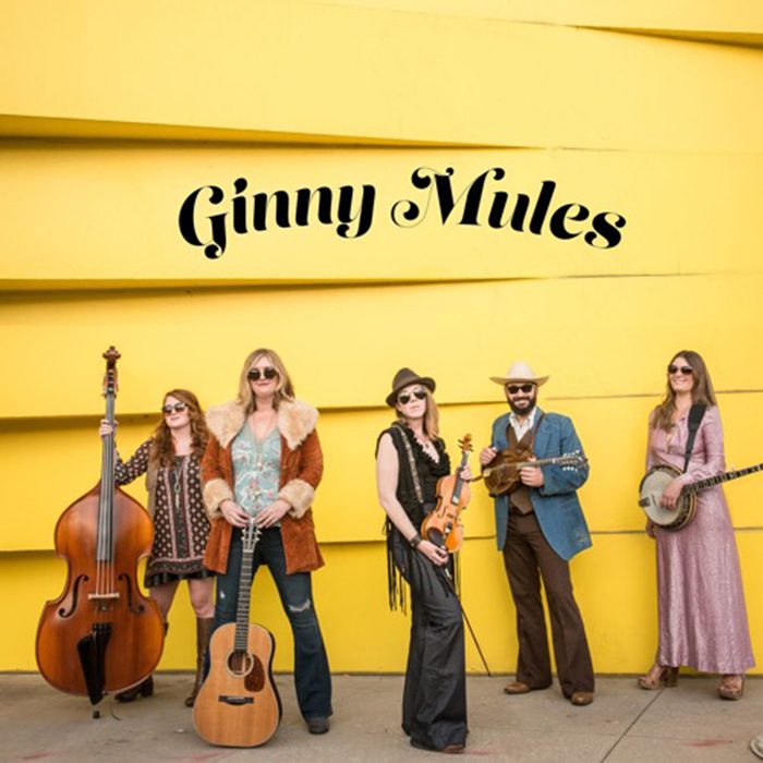 Band posing with instruments against yellow wall.