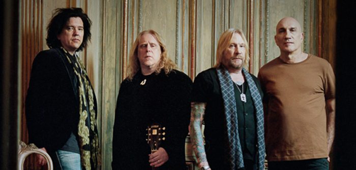 Four men standing in a row indoors.