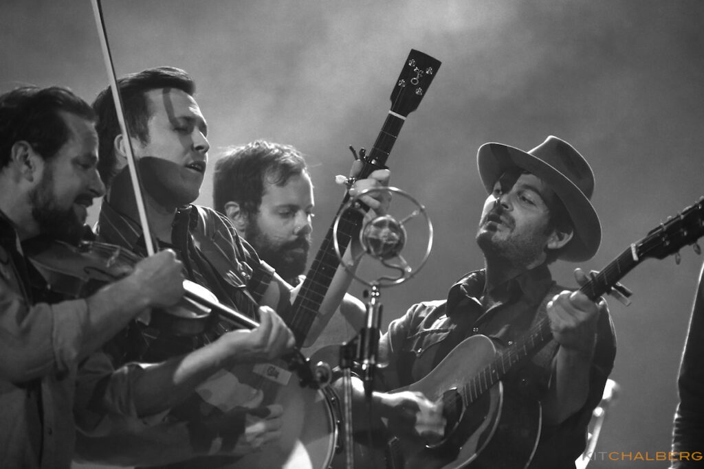 Band performing live with guitars and violin.