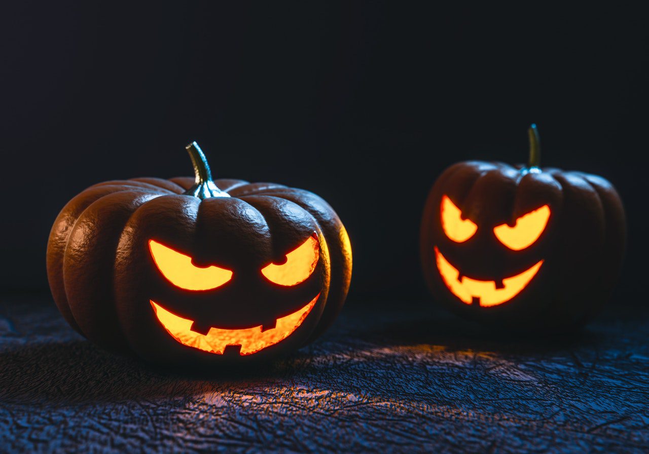 Two glowing carved Halloween pumpkins in darkness.