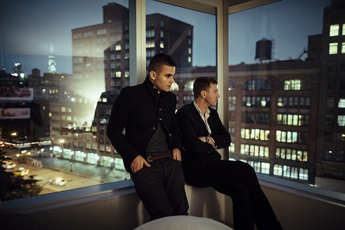 Two men gazing out cityscape window.