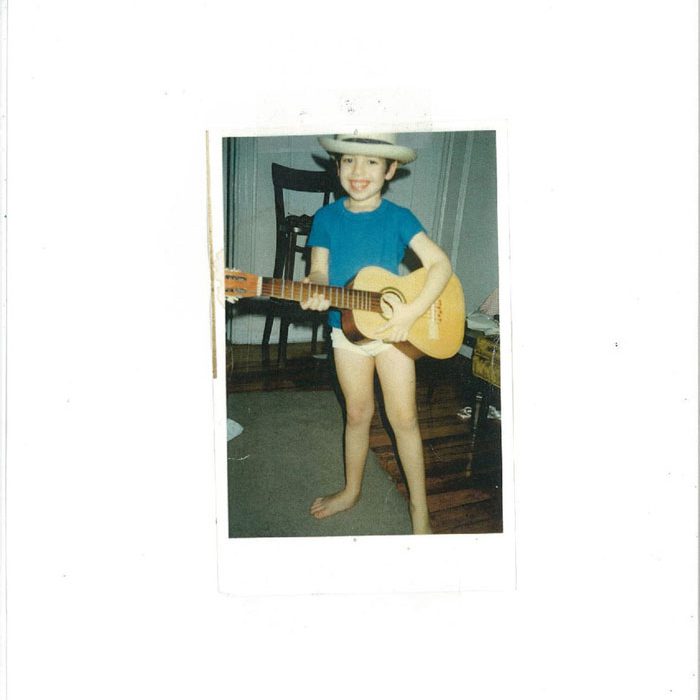 Child playing guitar wearing cowboy hat indoors.