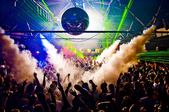 Crowded nightclub with lasers and smoke effects.