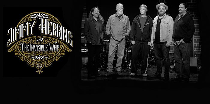 Band standing beside logo on dark background.