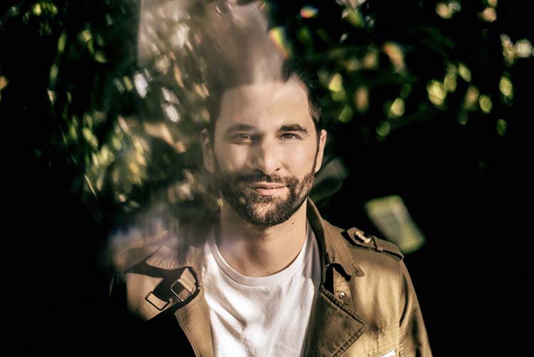 Man smiling in dappled sunlight, outdoors.