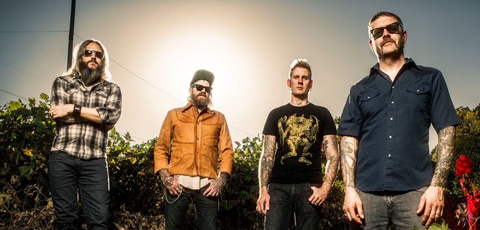Four men standing outdoors in sunlight.