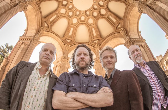 Four men standing under ornate dome.