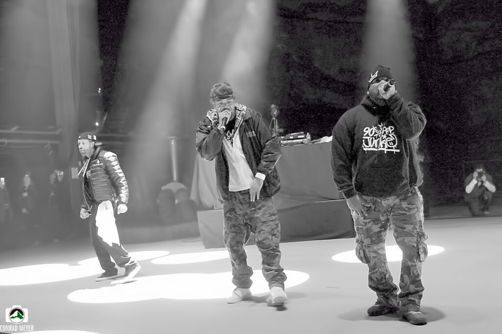 Rap group performing on stage under lights.