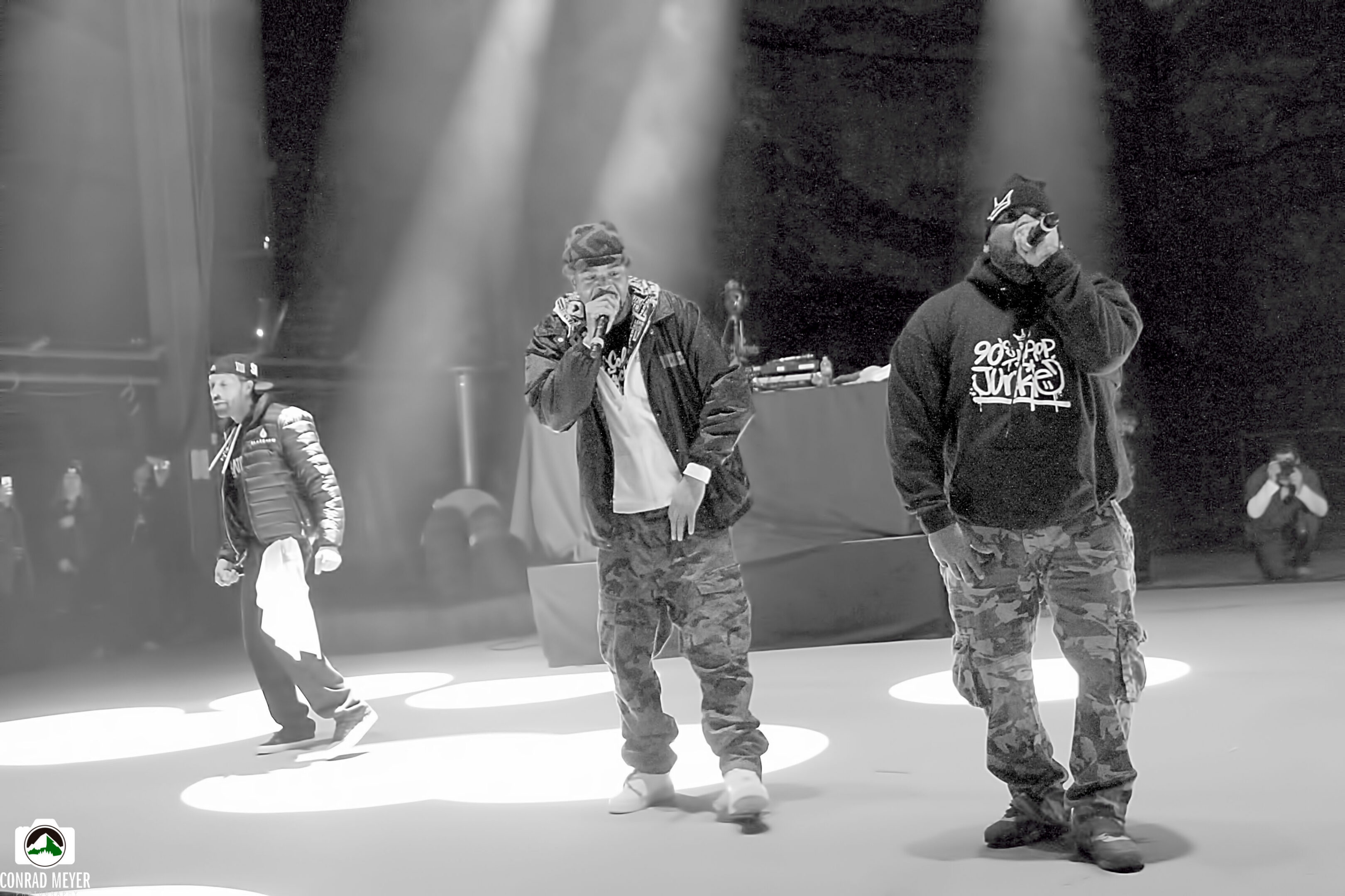 Rap group performing on stage under lights.