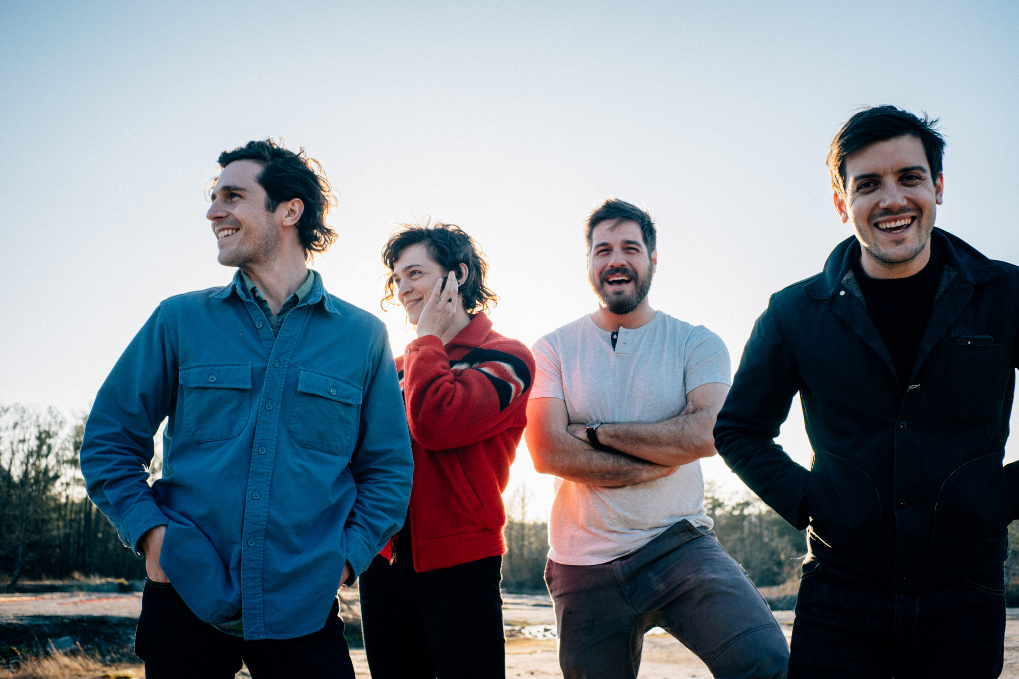 Four men smiling outdoors in daylight.
