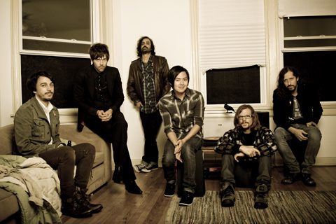 Six people sitting and standing in room.