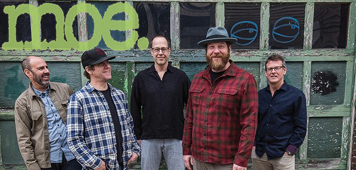 Five men standing in front of graffiti.