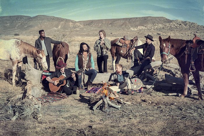 Group sitting by campfire with horses.