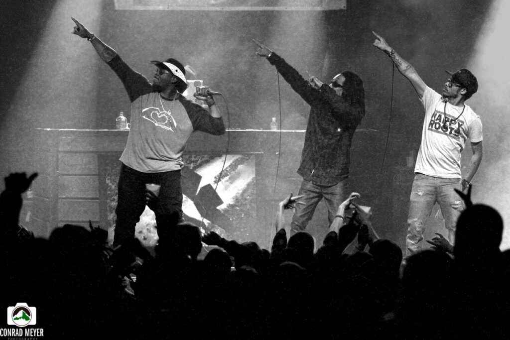 Three performers on stage pointing upward.