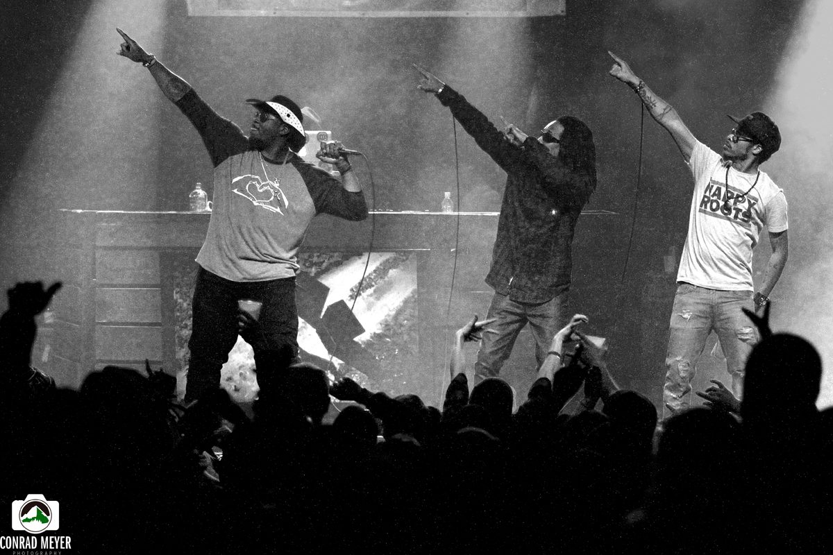 Three performers on stage pointing upward.