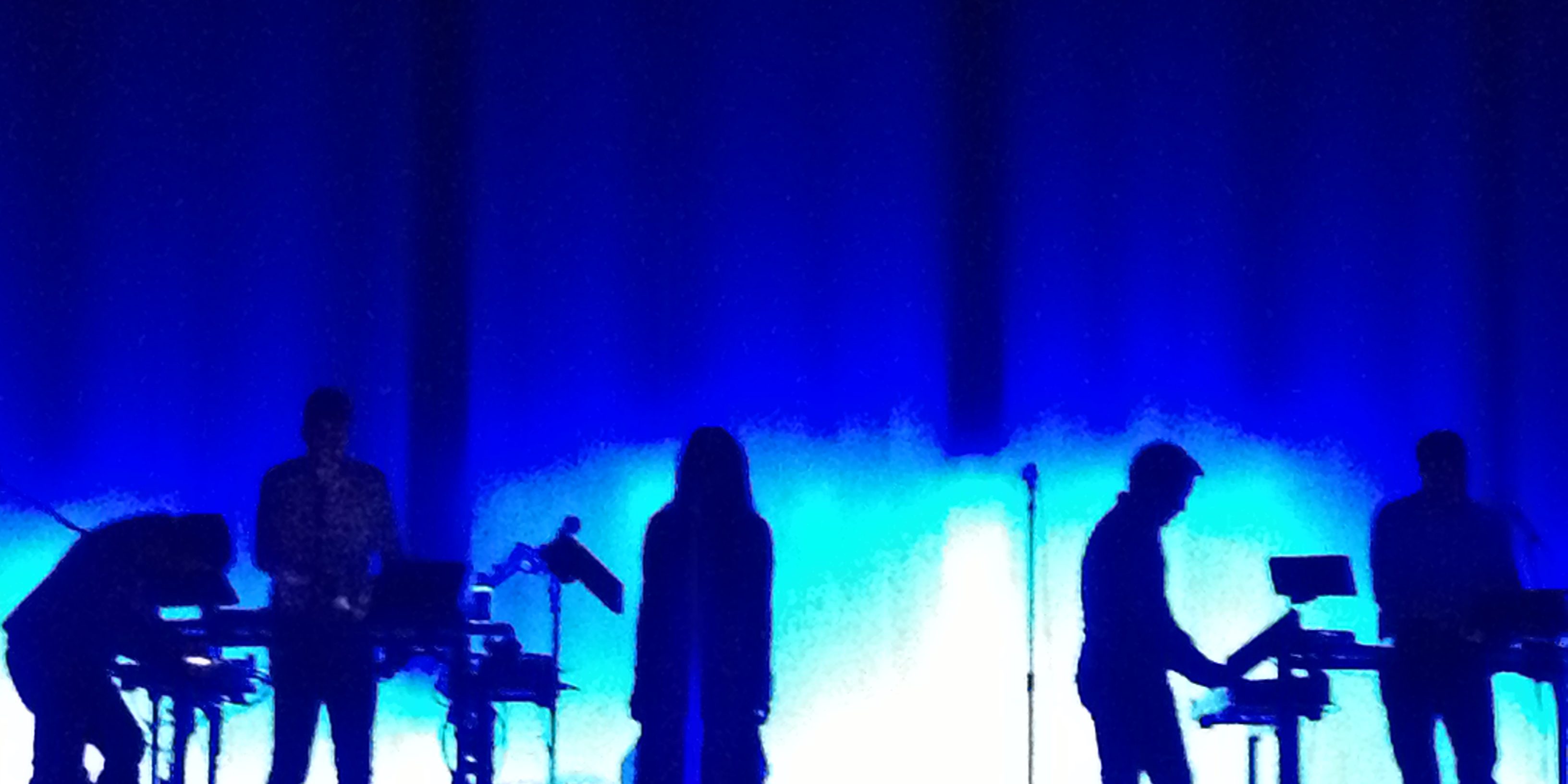 Silhouetted band performing on blue-lit stage.