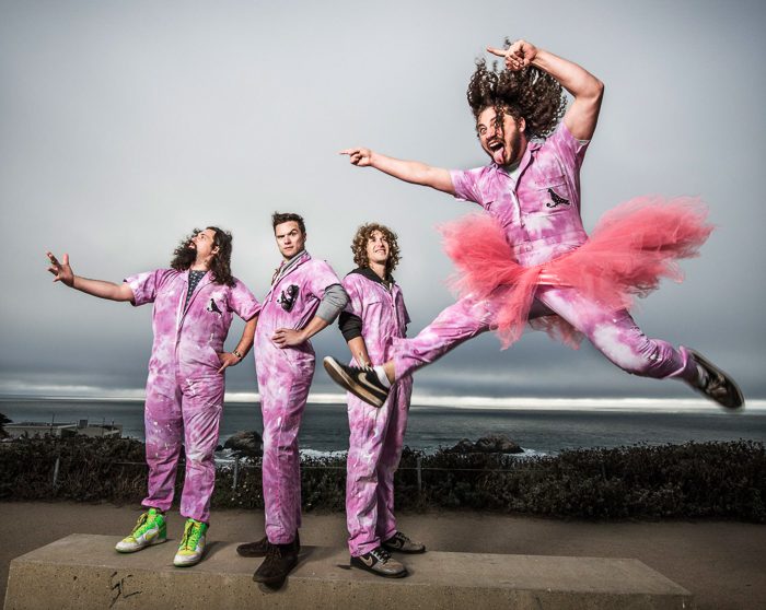Band in pink outfits, one jumping energetically.