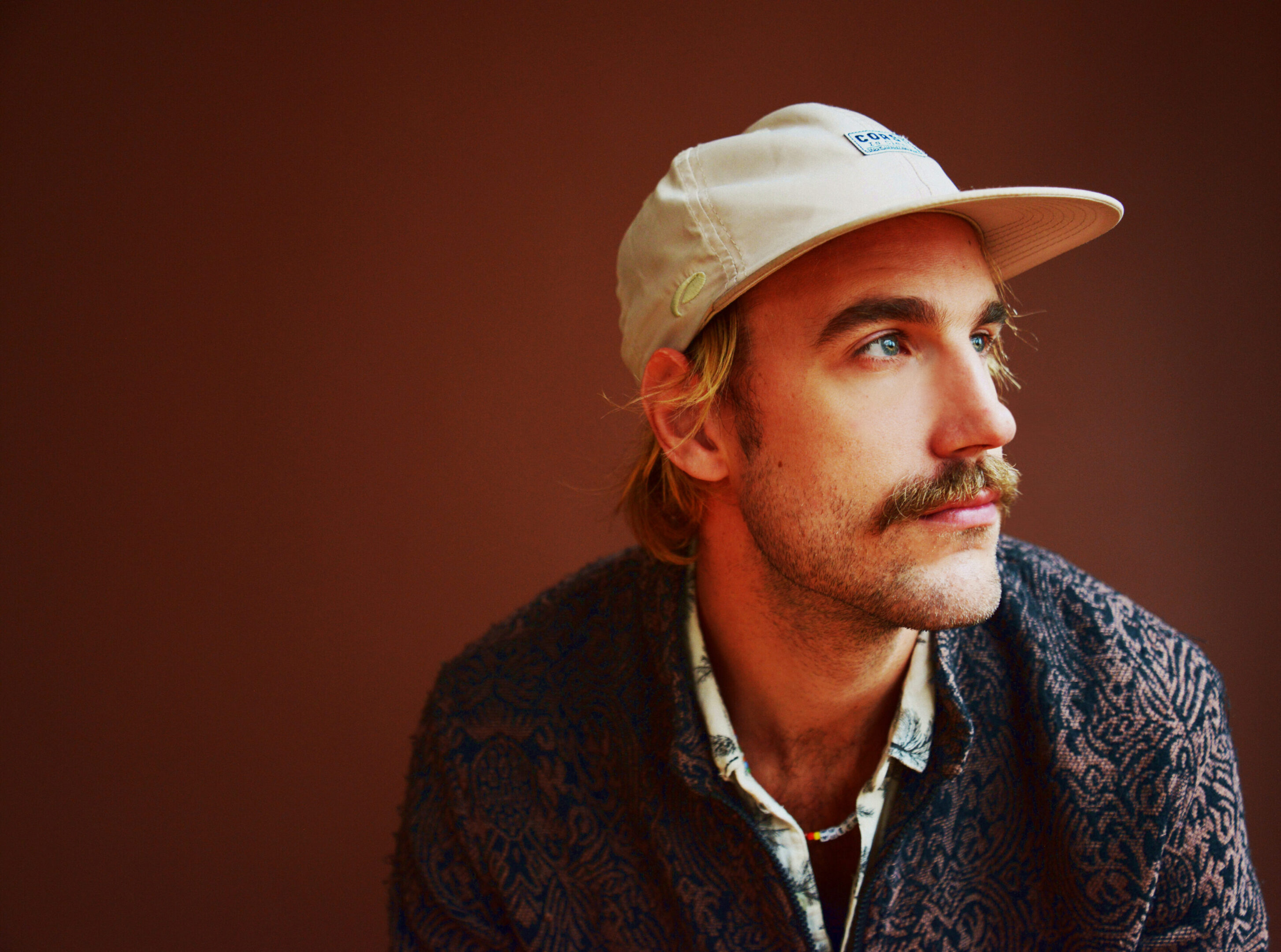 Man wearing cap and patterned shirt, looking sideways.
