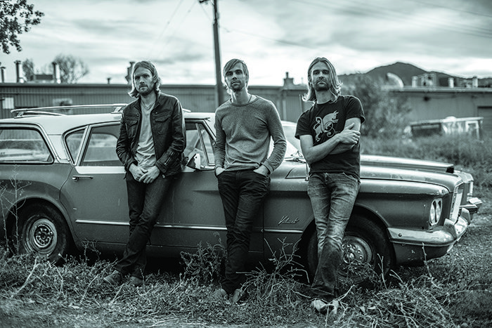 Three men leaning on vintage car outdoors.