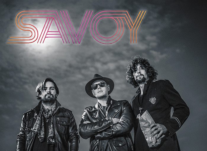Three men posing under "SAVOY" logo.