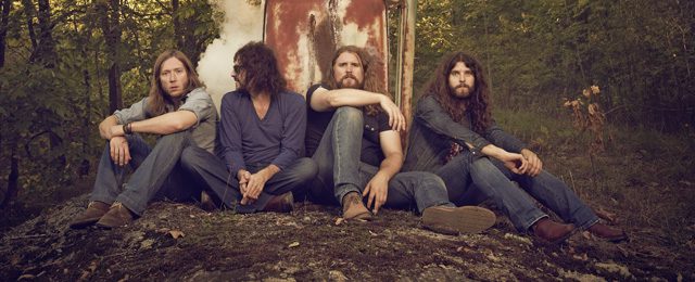 Four men sitting in a wooded area.