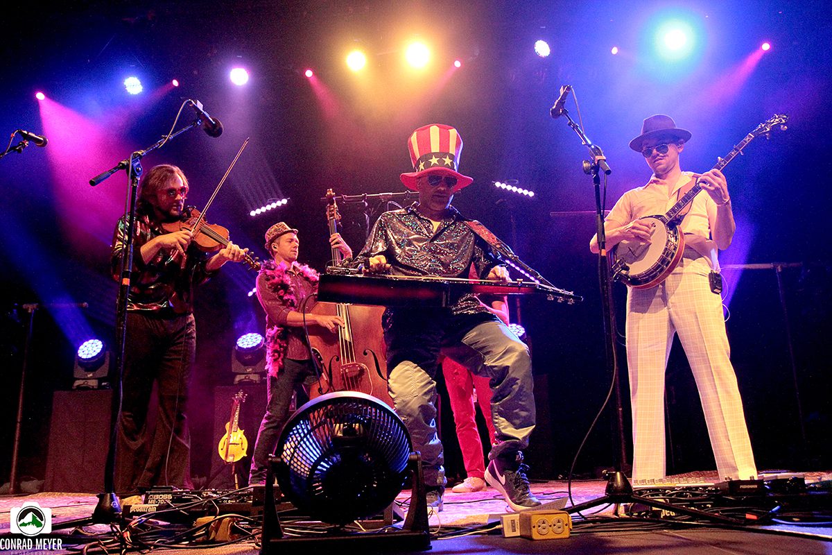 Band performing energetically on stage with instruments.