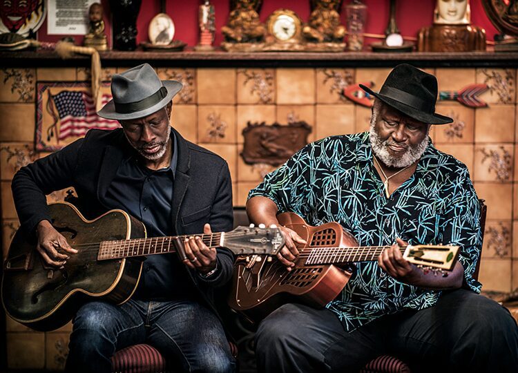 Two men playing guitars in a room.