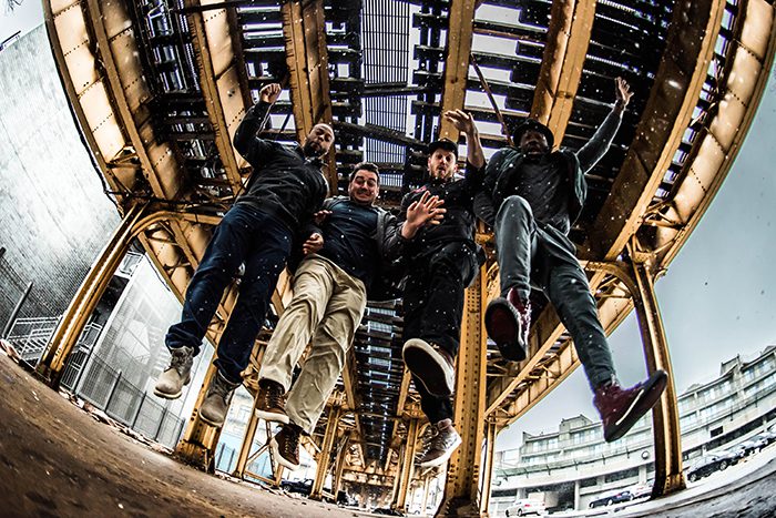 Four people jumping under a metal structure.