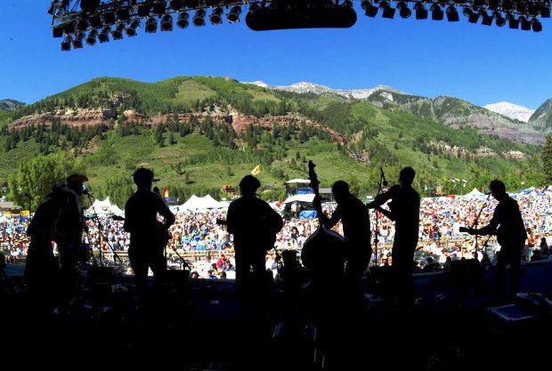 Silhouetted band performing at outdoor festival.