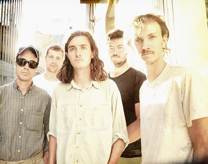 Five men standing in bright sunlight.