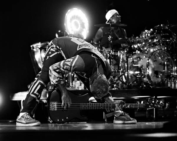 Musician bending over bass guitar on stage.