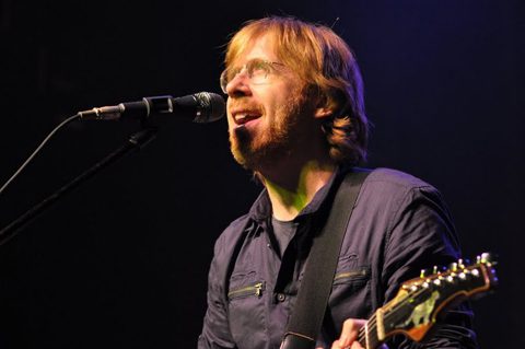 Musician singing and playing guitar on stage.