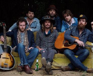 Band sitting with guitars on outdoor couch.