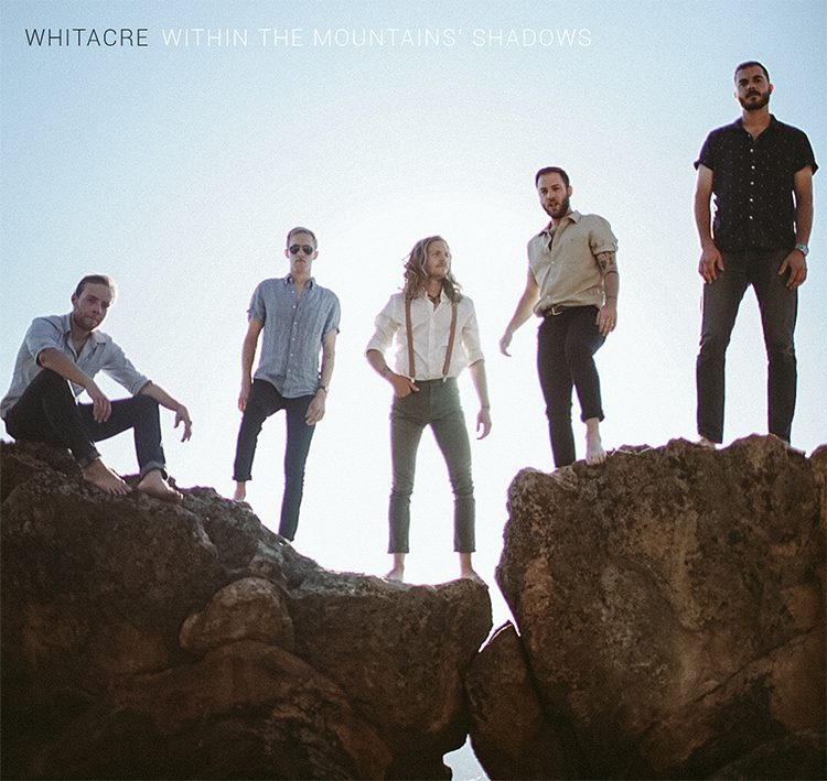 Band standing on rocks under blue sky.