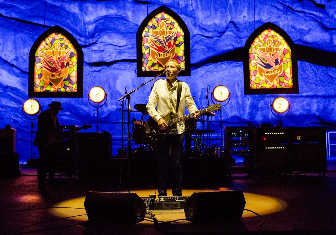 Musician performing on stage with stained glass backdrop.