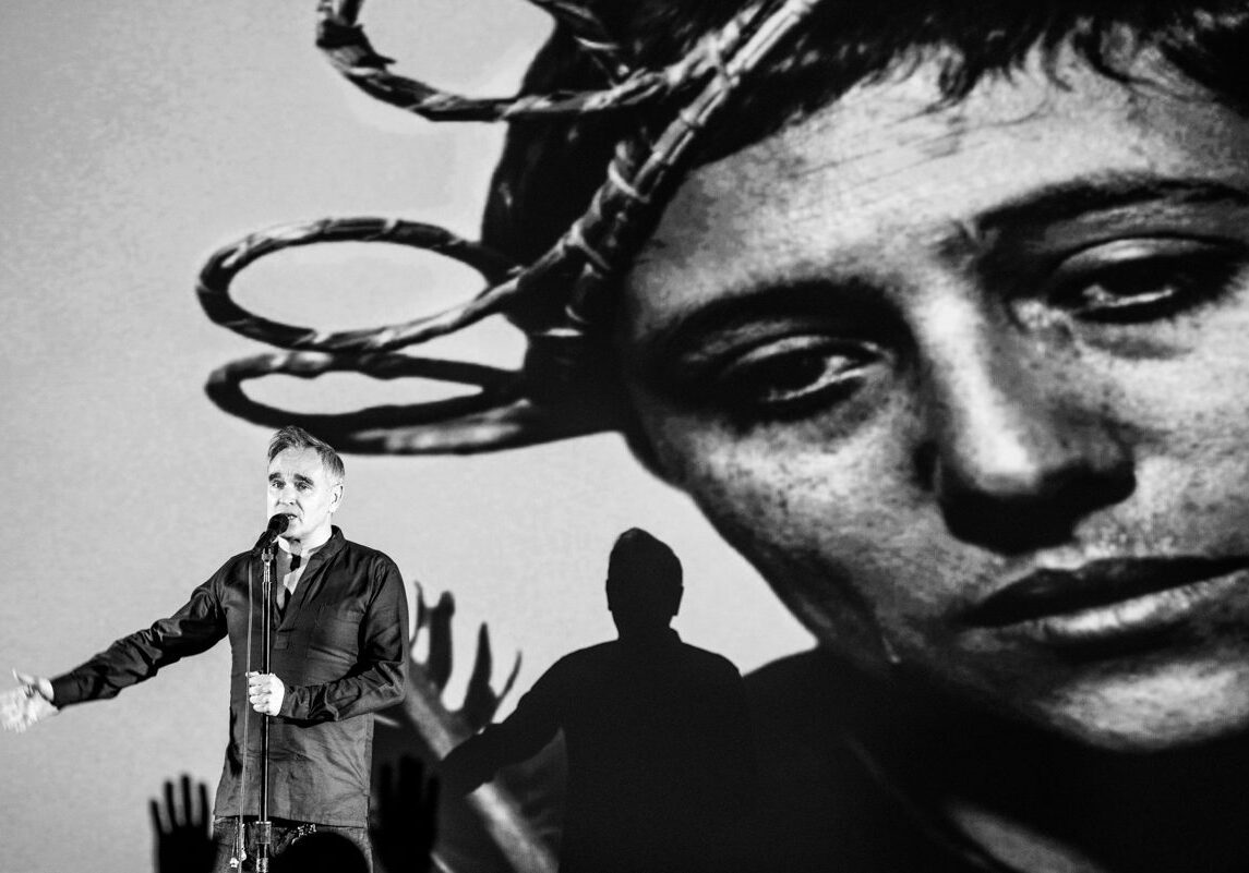Performer with microphone in front of projection.
