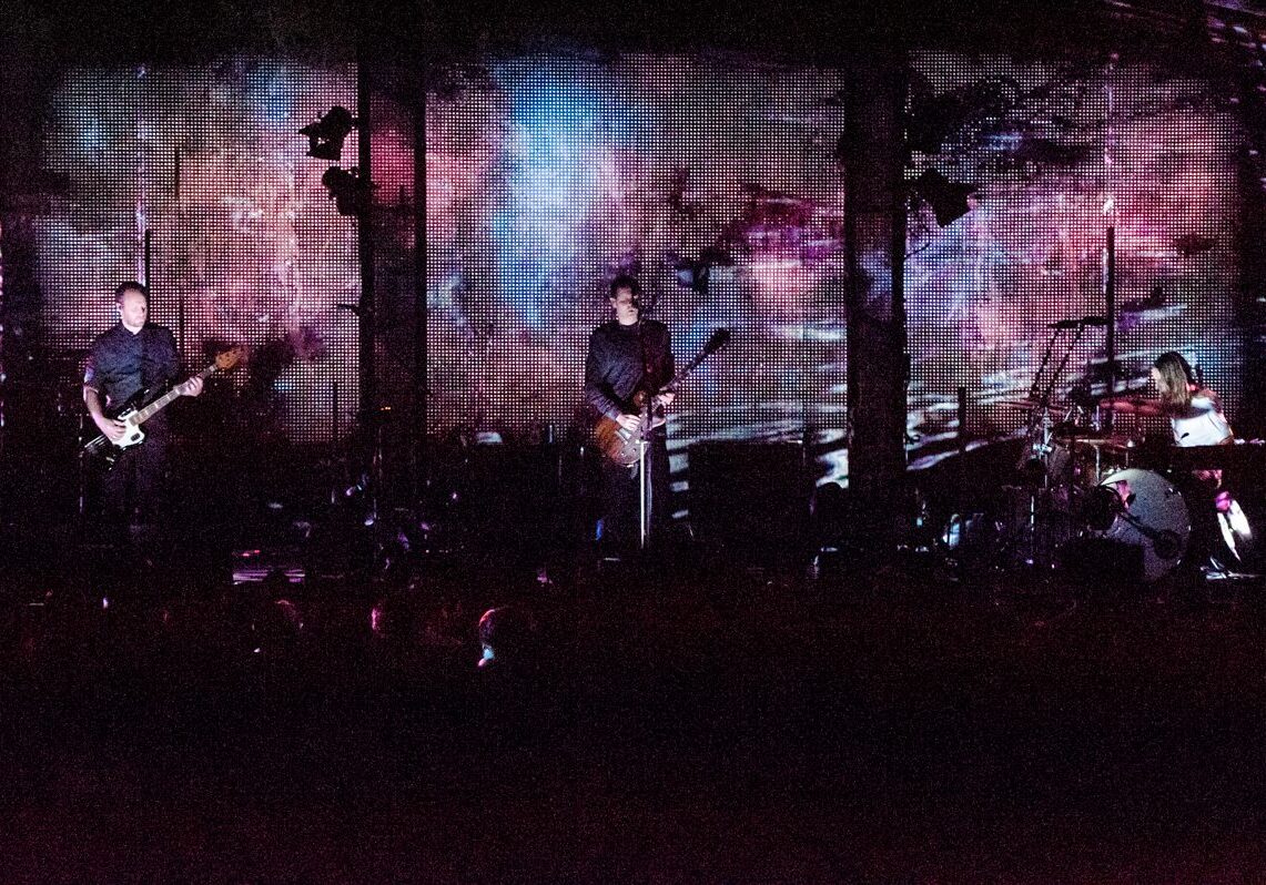 Band performing on stage with colorful backdrop.
