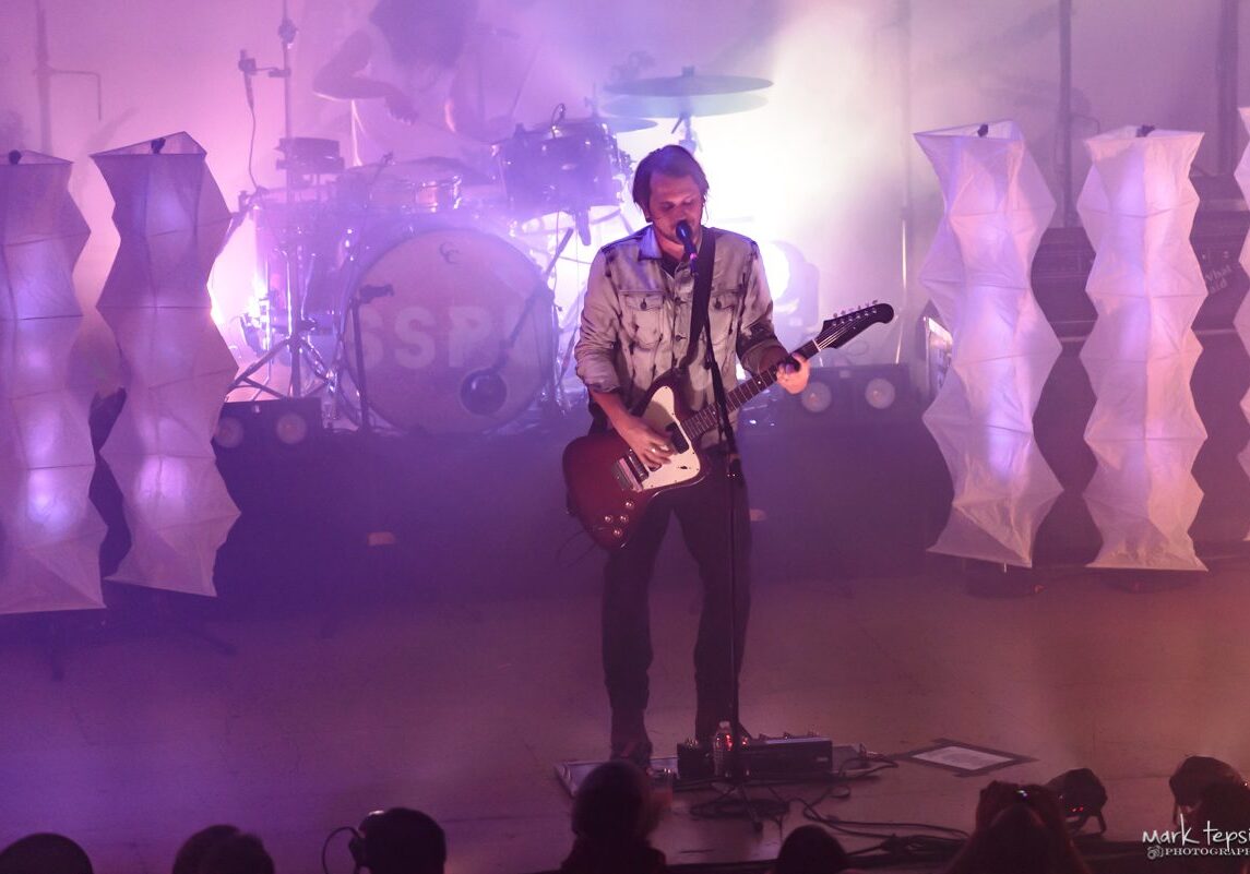Musician performing on stage with guitar.