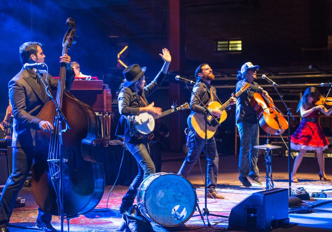 Band performing energetically on stage with instruments.