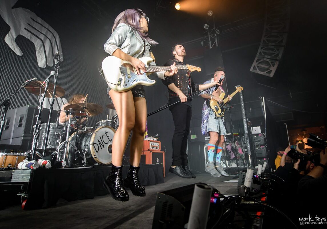 Band performing energetically on stage with instruments.
