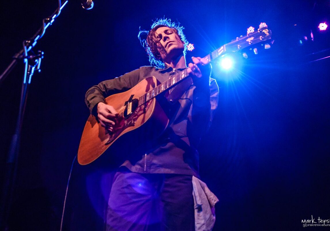 Musician performing with guitar on stage.