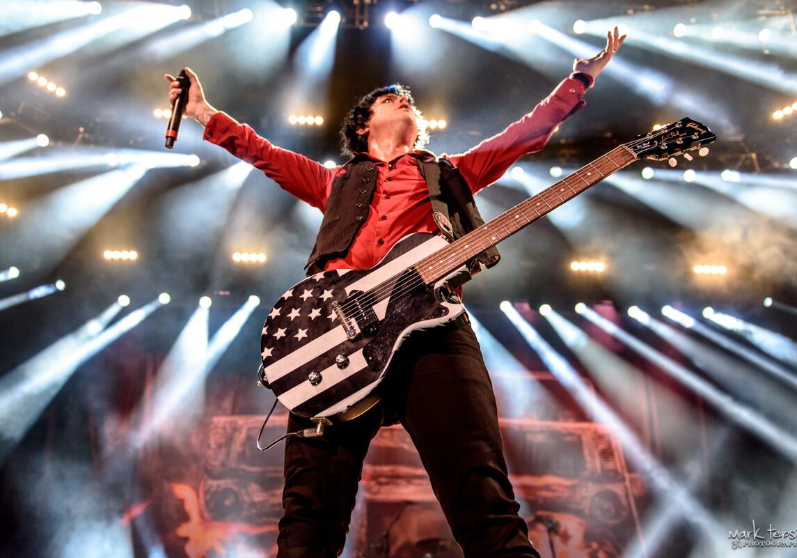 Musician performing energetically with guitar on stage.