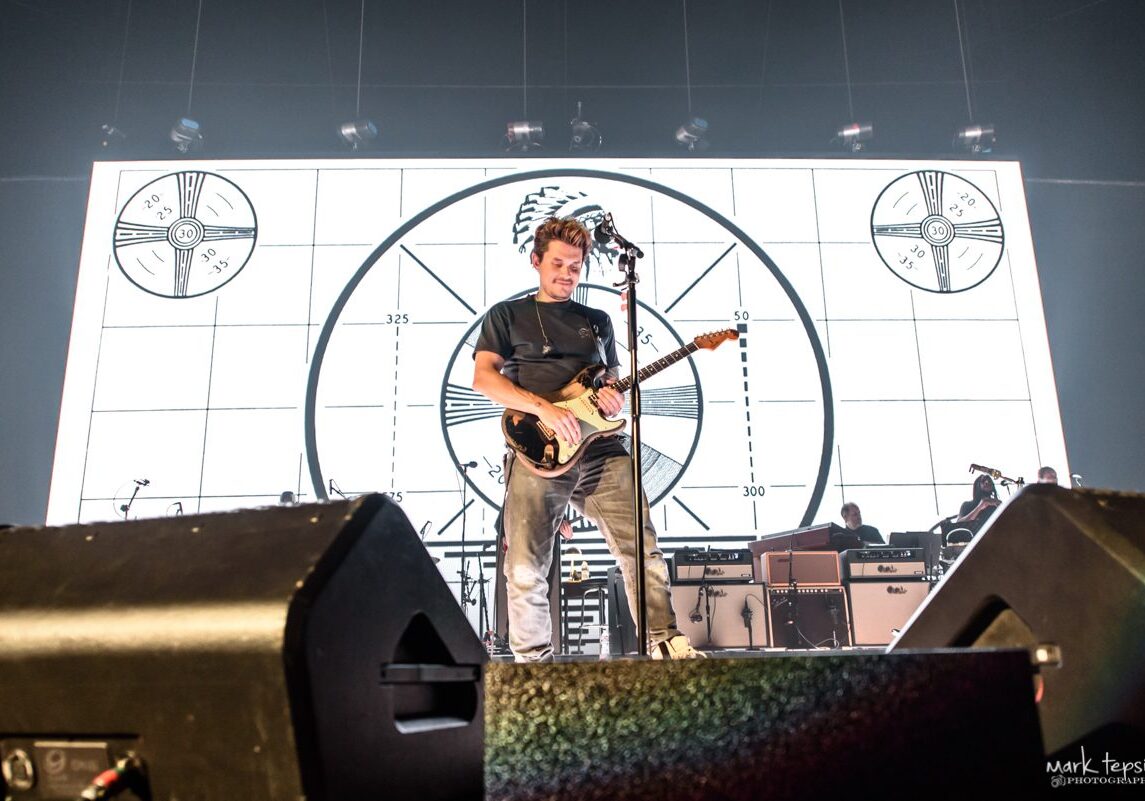 Guitarist performing on stage with visual backdrop.