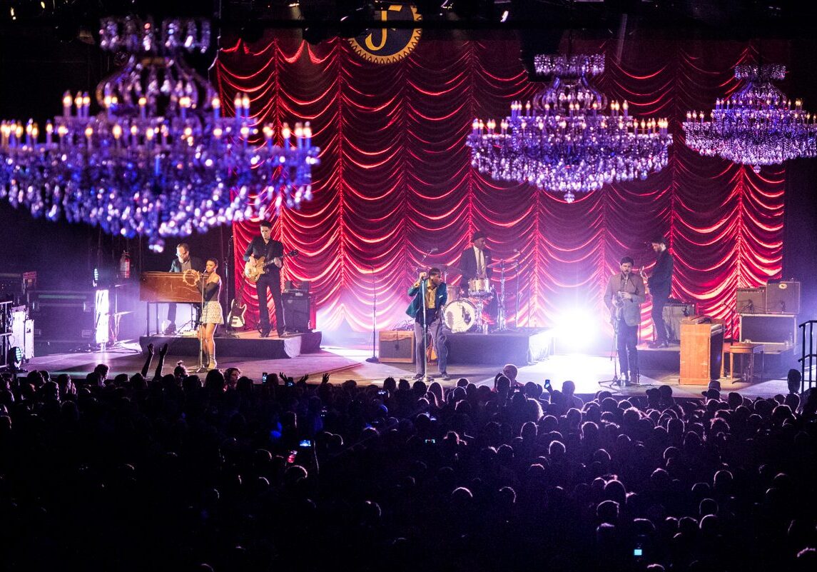 Band performing on stage with chandeliers above.