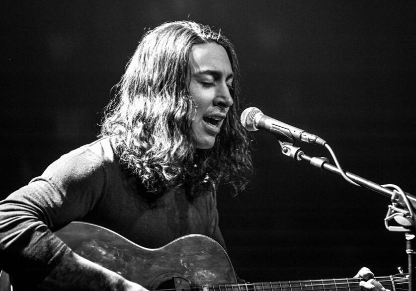 Musician singing and playing guitar on stage.